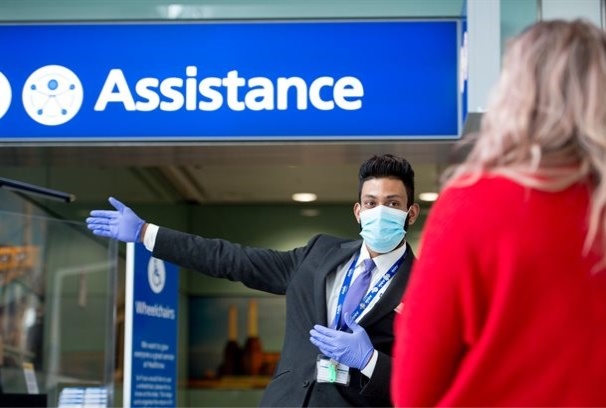A man wearing a facemask and gloves at Heathrow airport offering passenger assistance